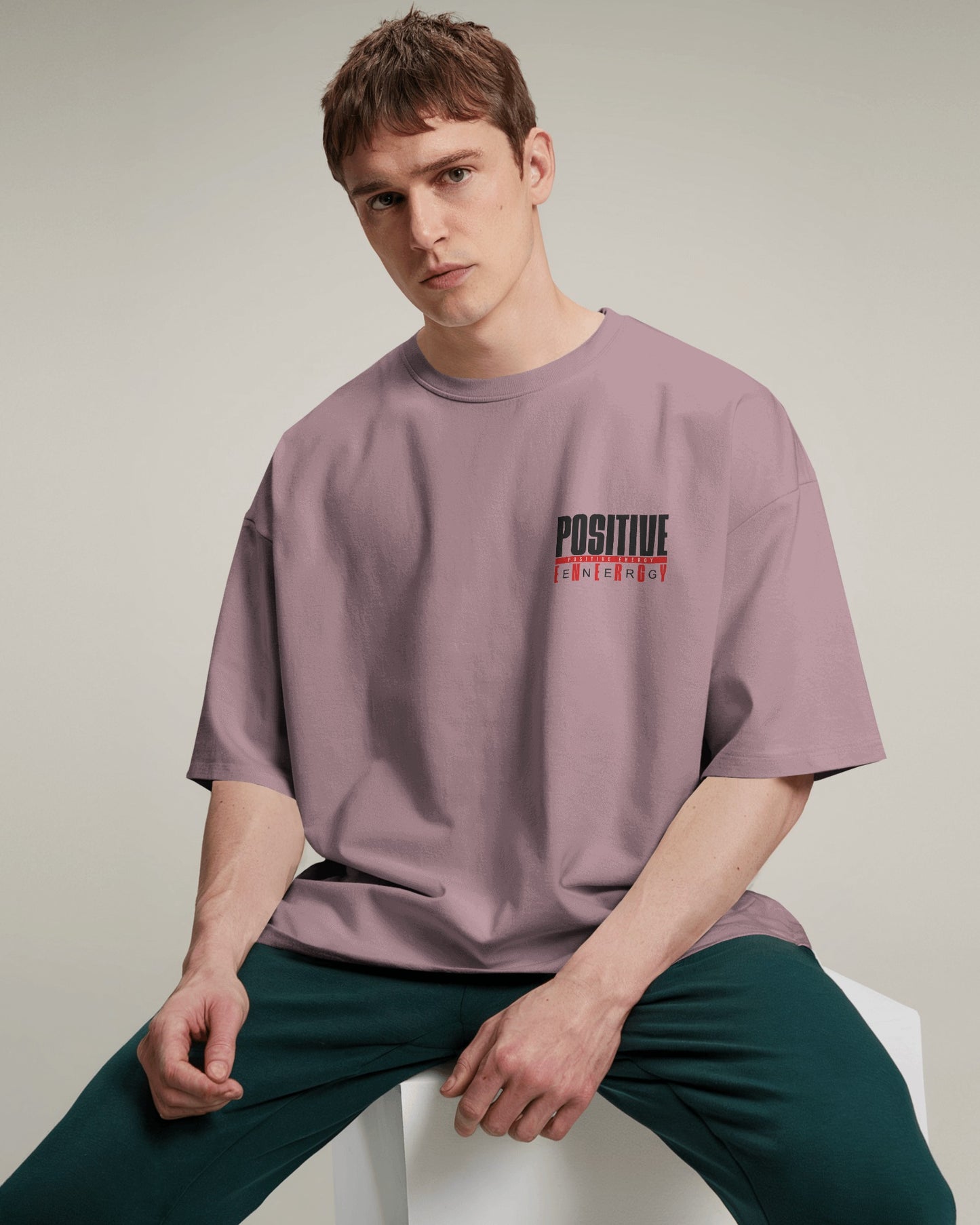 Man wearing a purple t-shirt with text sitting on a white chair against a beige background