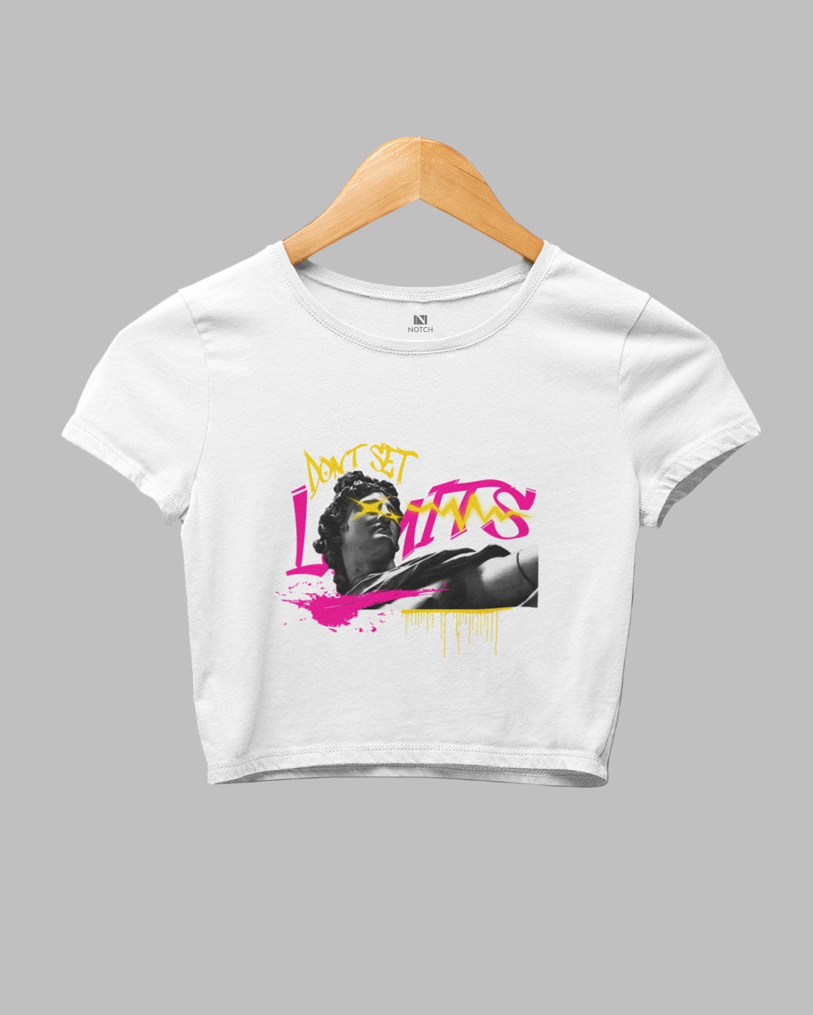 White crop top with graphic design on a hanger against a dark background